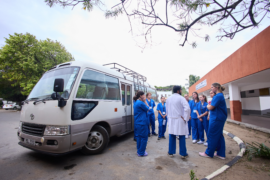 A group of people, some in blue scrubs, stand near a bus talking to a person in a white coat. Possibly related to occupational therapy internships.