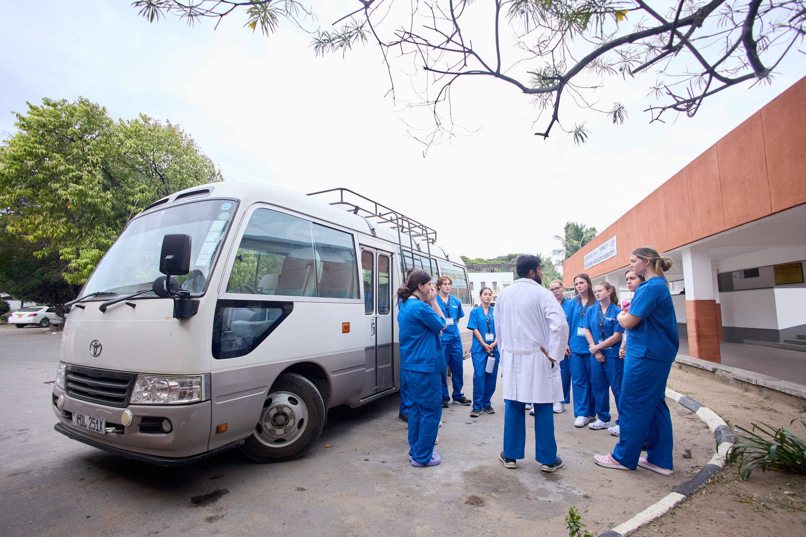 A group of people, some in blue scrubs, stand near a bus talking to a person in a white coat. Possibly related to occupational therapy internships.