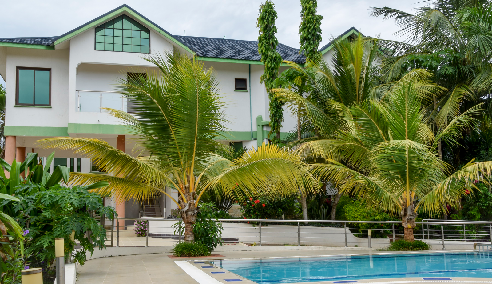 A white two-story house surrounded by palm trees, with a swimming pool in the foreground.