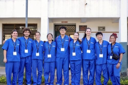 Group of physician assistant and pre-PA interns in matching blue scrubs smiling outside a clinical training facility.