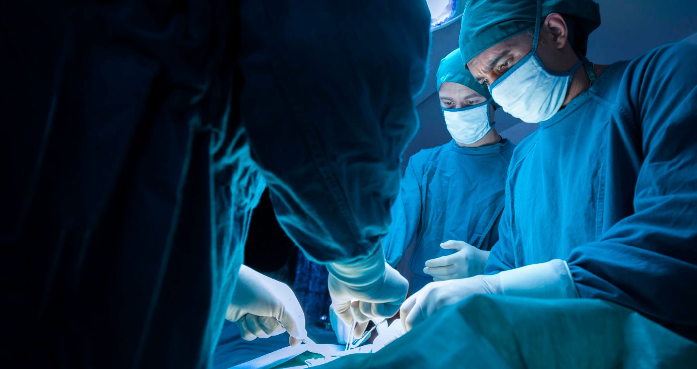 Surgeons performing an operation in a well-lit operating room, wearing surgical attire and masks.
