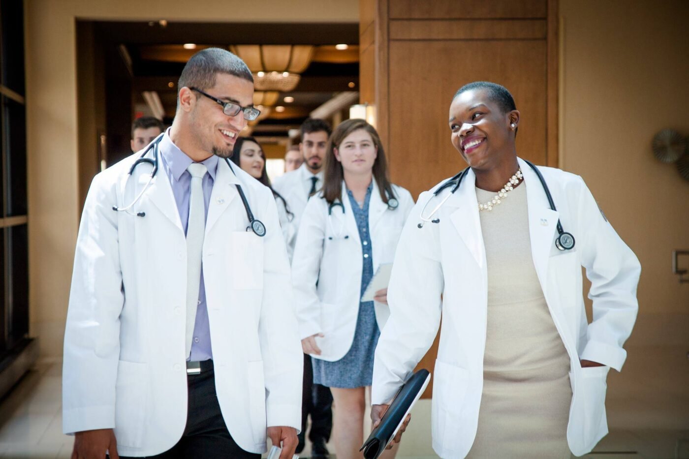 A group of people in white coats, likely medical professionals or students, walking and smiling.
