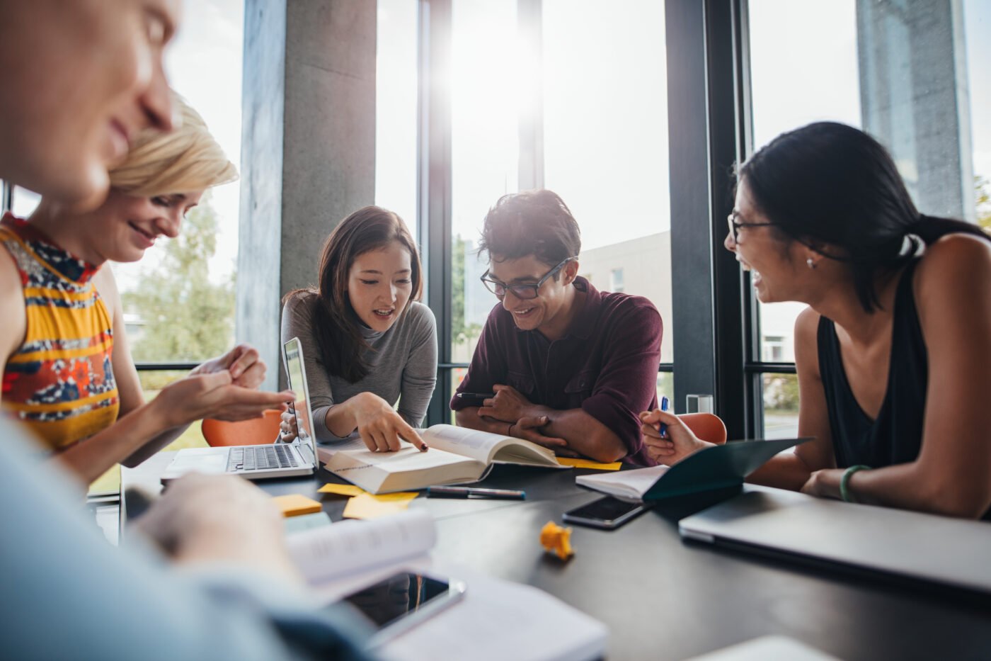 A group of people are gathered around a table, collaborating and discussing, with notes and a laptop.