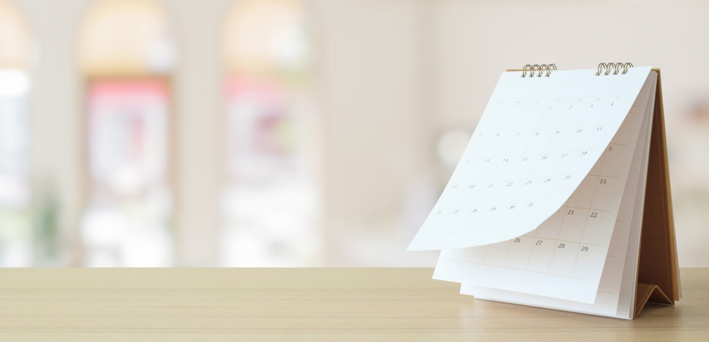 A spiral-bound desk calendar on a table, with a blurred background. Related to MCAT test dates.