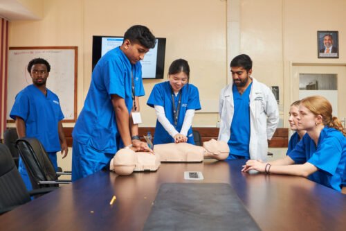 A group of medical professionals in blue scrubs practicing CPR on mannequins in a classroom setting.