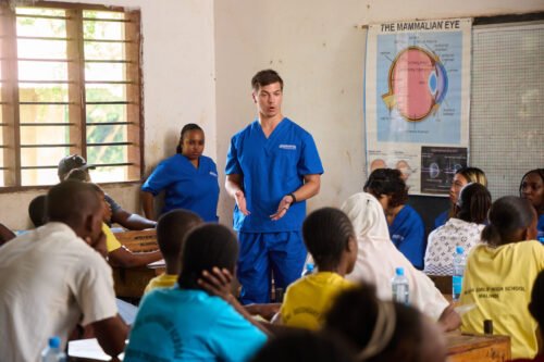 A group of people in a classroom setting, likely discussing medical topics. There's a poster of the mammalian eye on the wall.