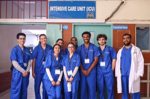 A group of people in blue scrubs posing in front of an intensive care unit sign