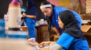 People in blue uniforms are working together, possibly organizing supplies or discussing tasks.