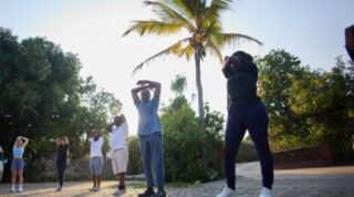 People are stretching outdoors under a palm tree, engaging in physical exercise.