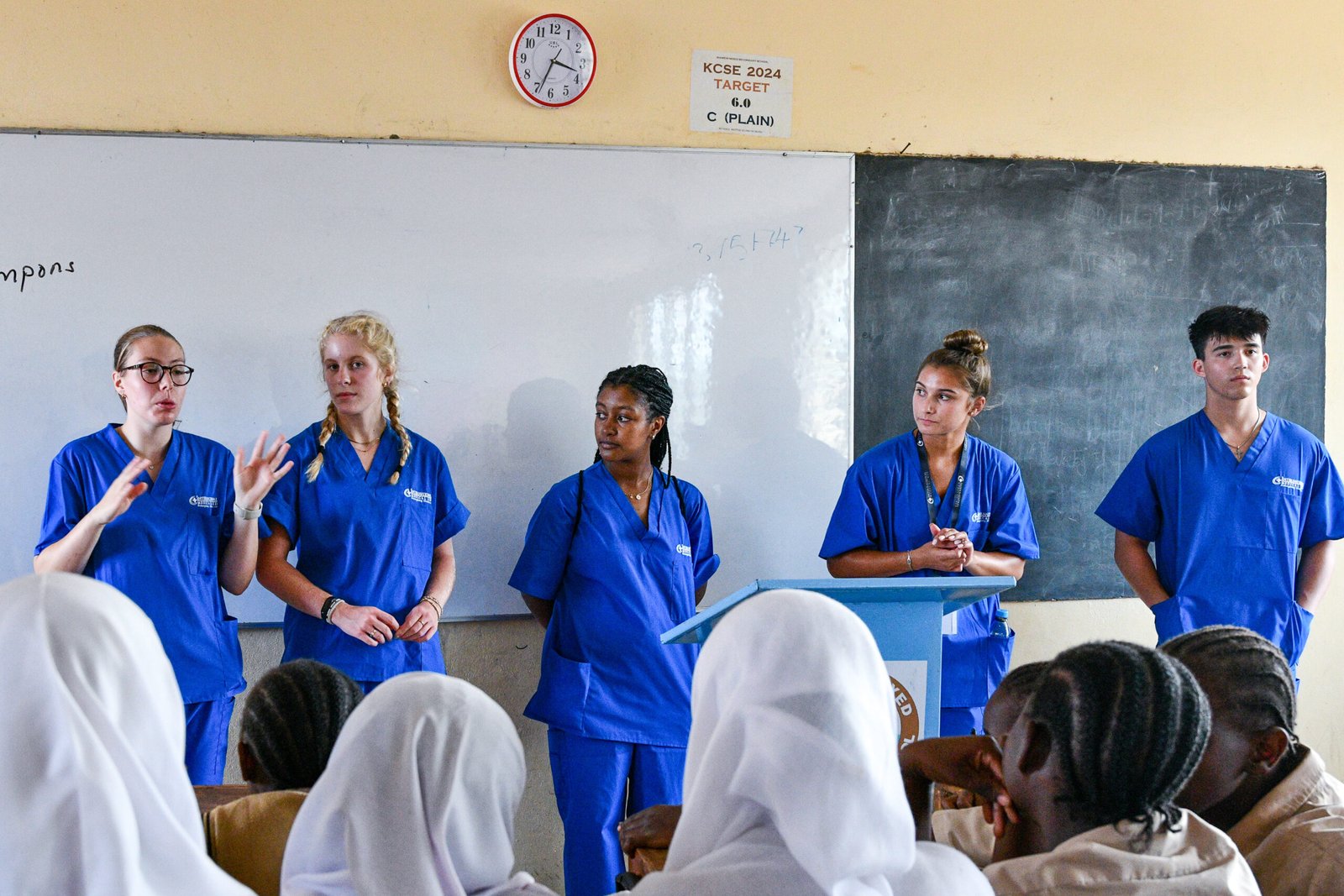 A group of people in blue scrubs presenting to an audience in a classroom, possibly related to medical topics.
