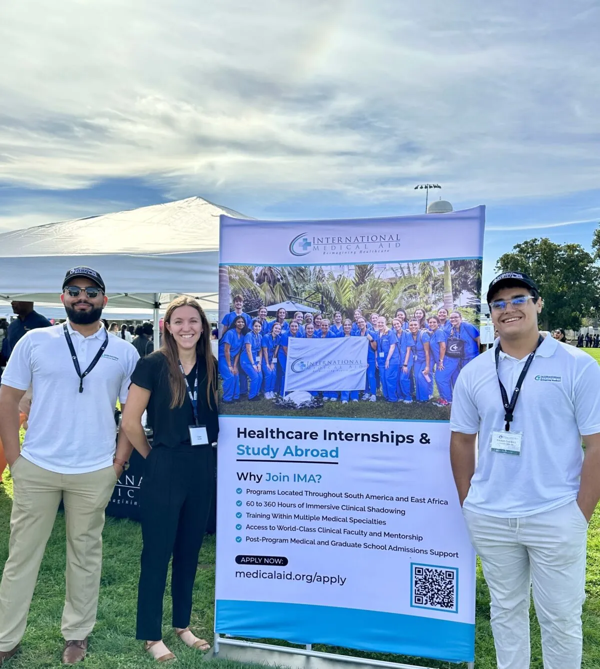 Three representatives standing beside a promotional banner for international healthcare internships and study abroad opportunities at an outdoor event.