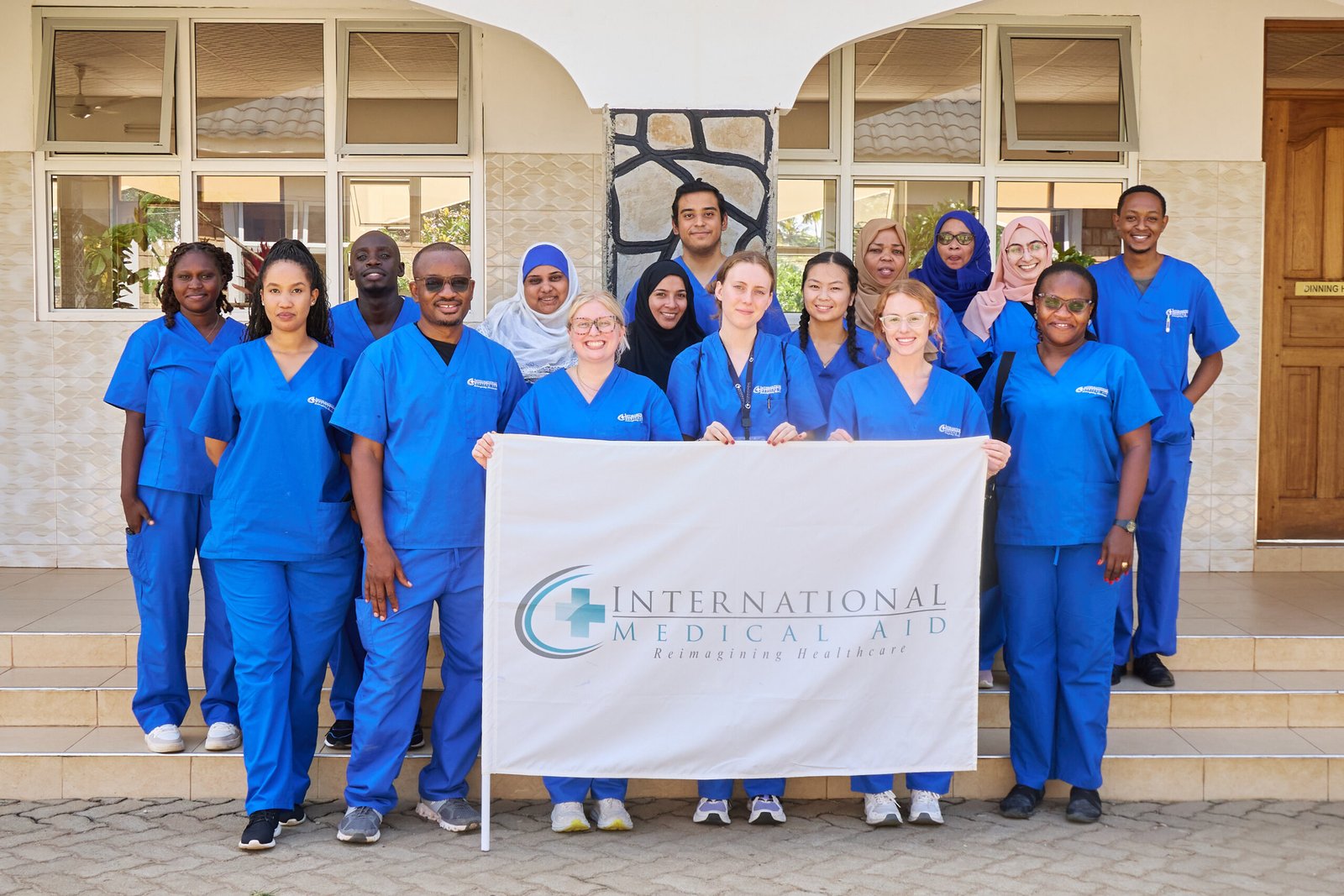 A group of individuals in blue scrubs standing together, holding a banner for International Medical Aid.