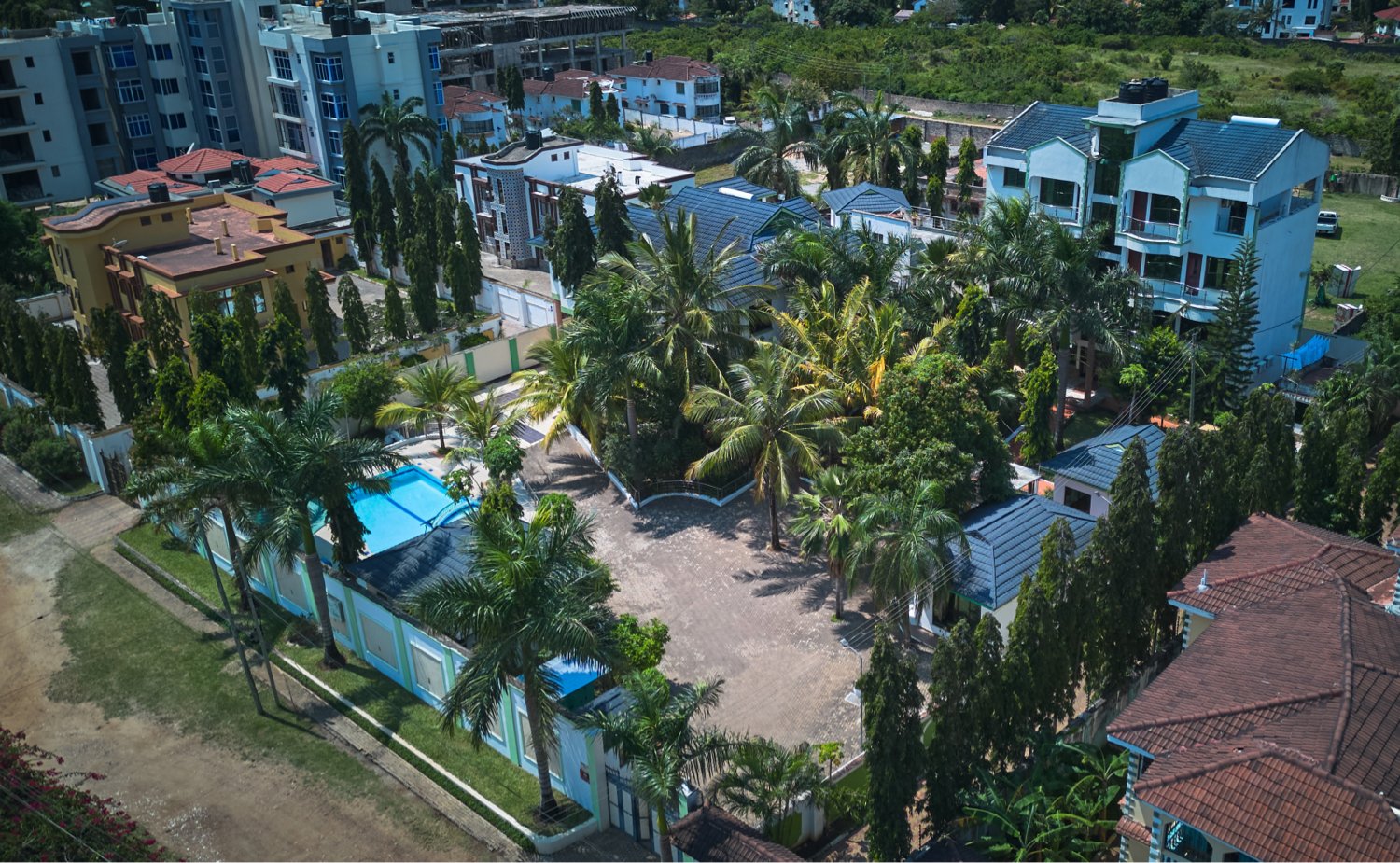 Aerial view of a residential area with houses, a pool, trees, and nearby buildings.