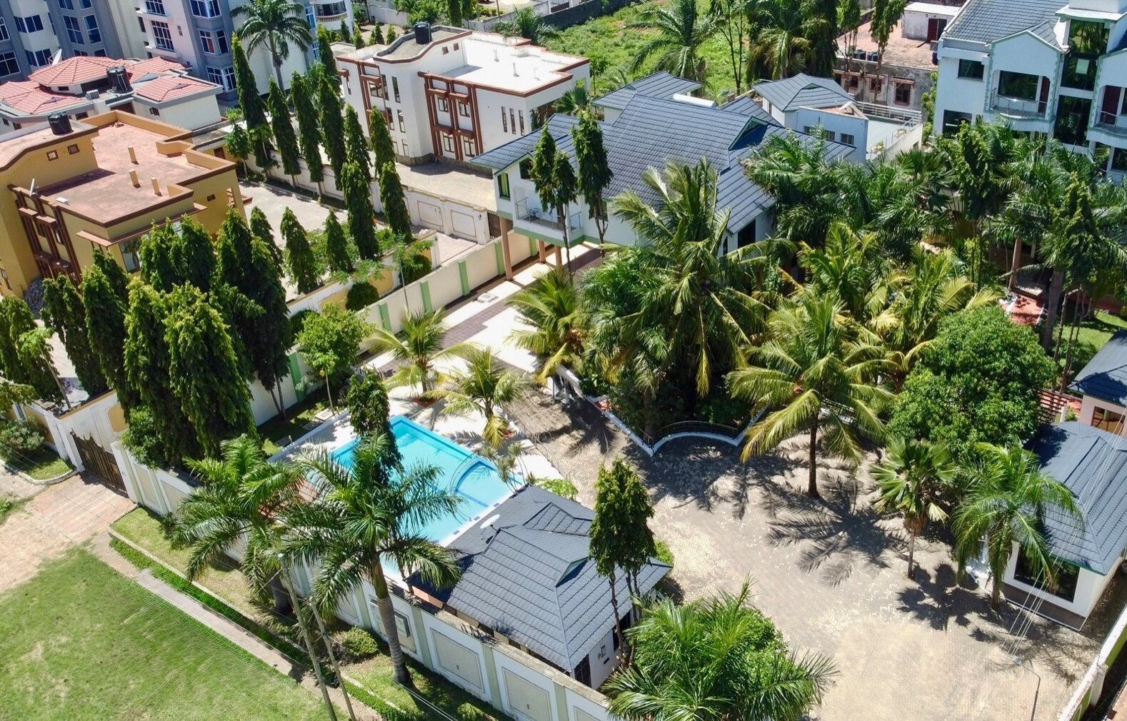 Aerial view of a residential area with a swimming pool, palm trees, and several houses.