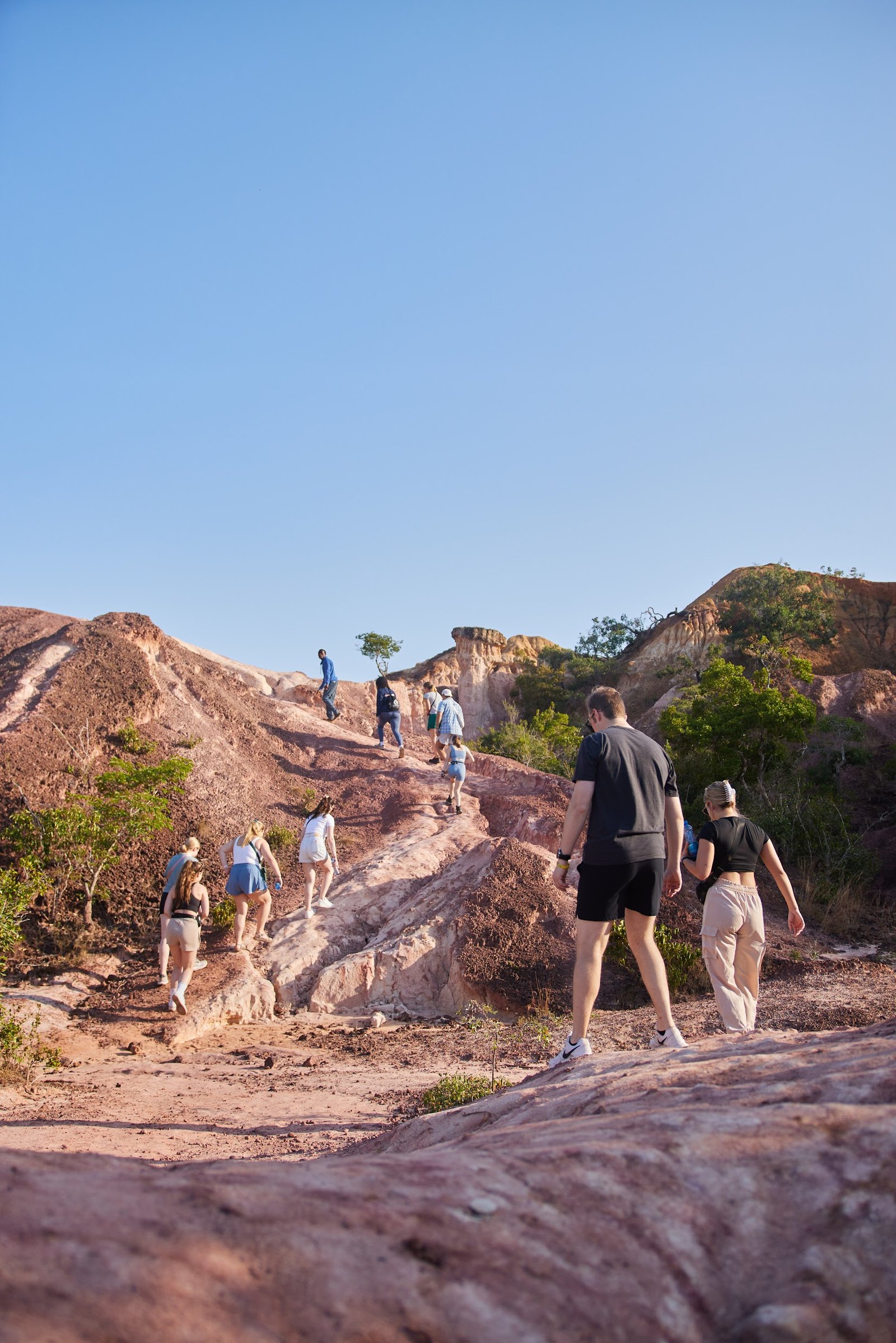 A group of people are hiking up a rocky, barren hill on a sunny day.