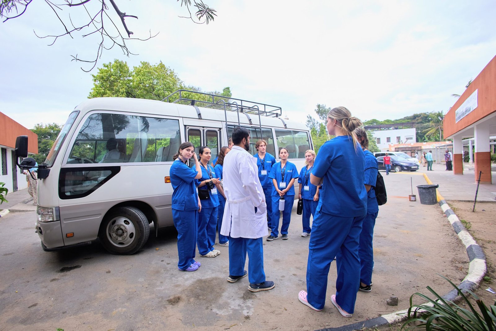 A group of people in blue scrubs stands near a bus, with one person in a white coat, likely discussing healthcare activities.