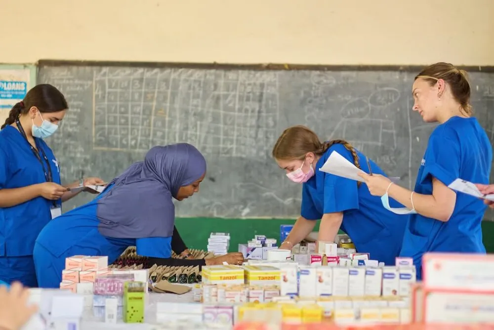 Medical interns in blue scrubs organizing and labeling medications on a table in a classroom.