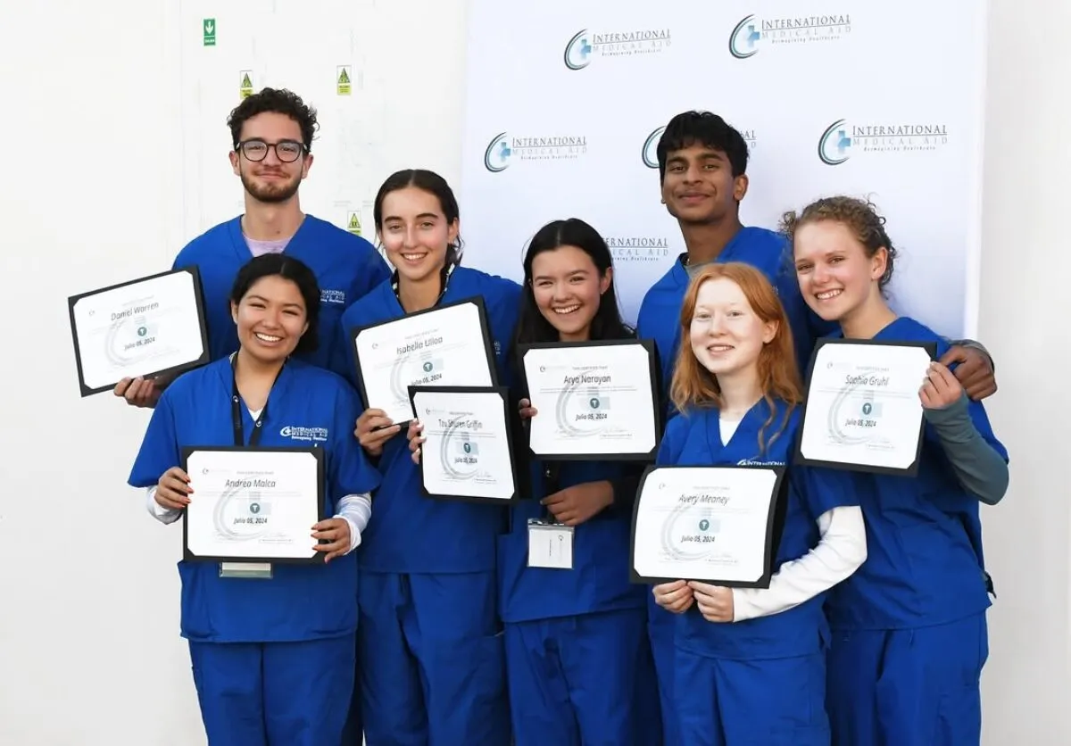 Three people in blue scrubs are holding certificates from International Medical Aid, celebrating an achievement.