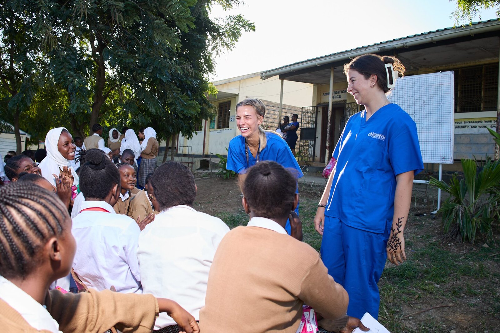 Two people in blue scrubs engaging with a group outdoors.