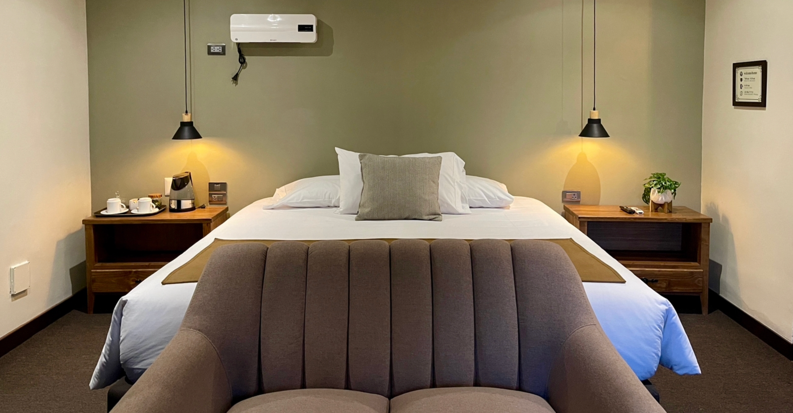 A cozy bedroom with a double bed, nightstands, pendant lights, a sofa, and an air conditioner.