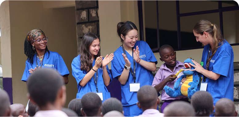 A group of people in blue attire is standing in front of an audience, engaging with a child holding a toy.
