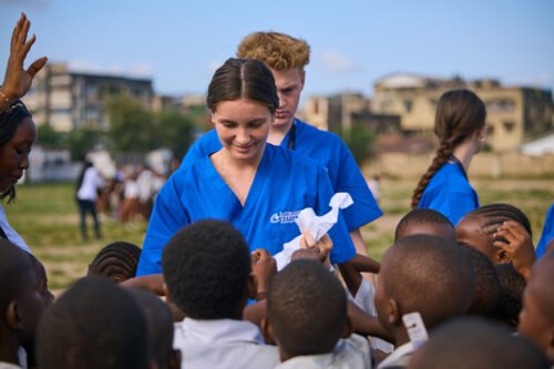 A group of people in blue uniforms are interacting with children outdoors.