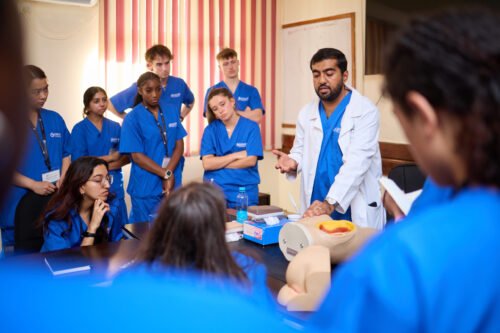 A group of people in blue scrubs are gathered around a person in a lab coat, possibly in a medical training session.