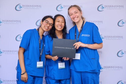 Three people in blue scrubs holding a certificate from International Medical Aid and smiling at the camera.