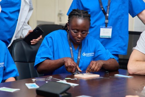 A person in blue scrubs is practicing surgical skills with instruments.