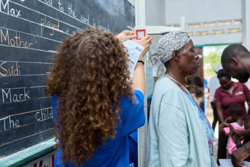 A person measures an elderly woman’s height in a classroom setting.