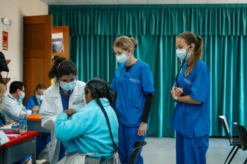 A group of medical professionals and students, in scrubs and masks, attending to a patient in a clinical setting.